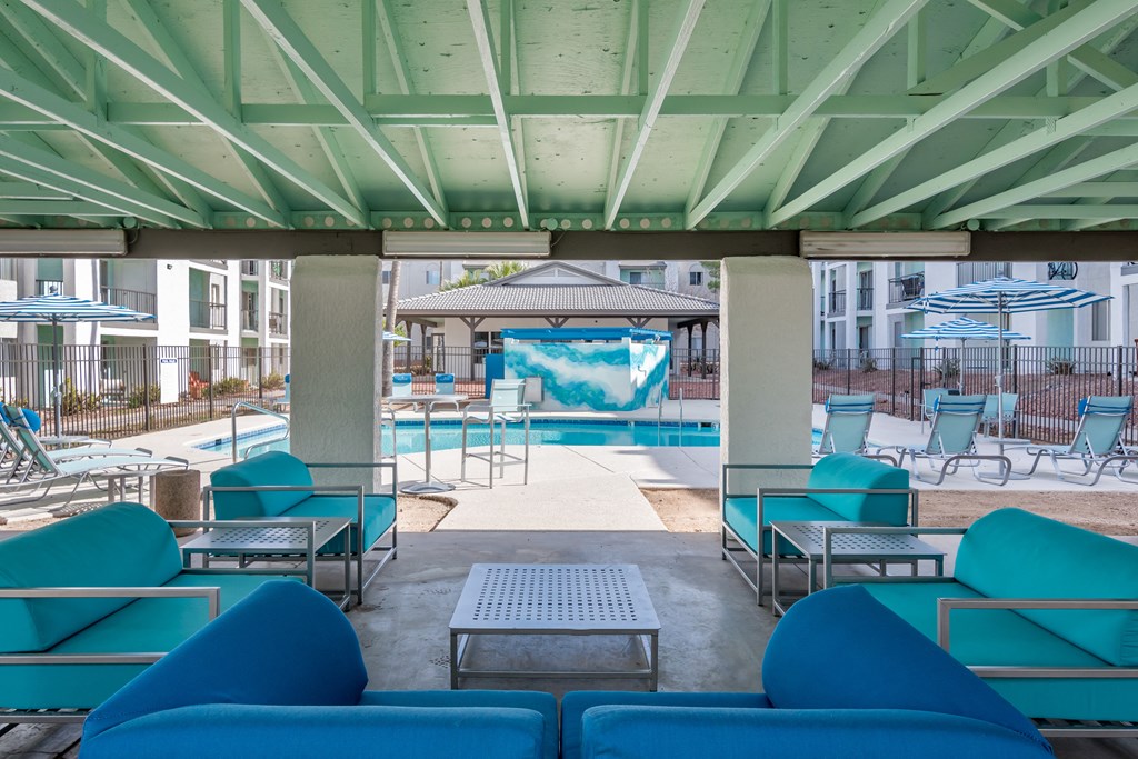 a lounge area with blue couches and chairs and a pool in the background