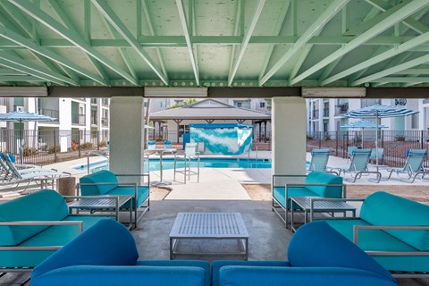 a lounge area with blue couches and chairs and a pool in the background