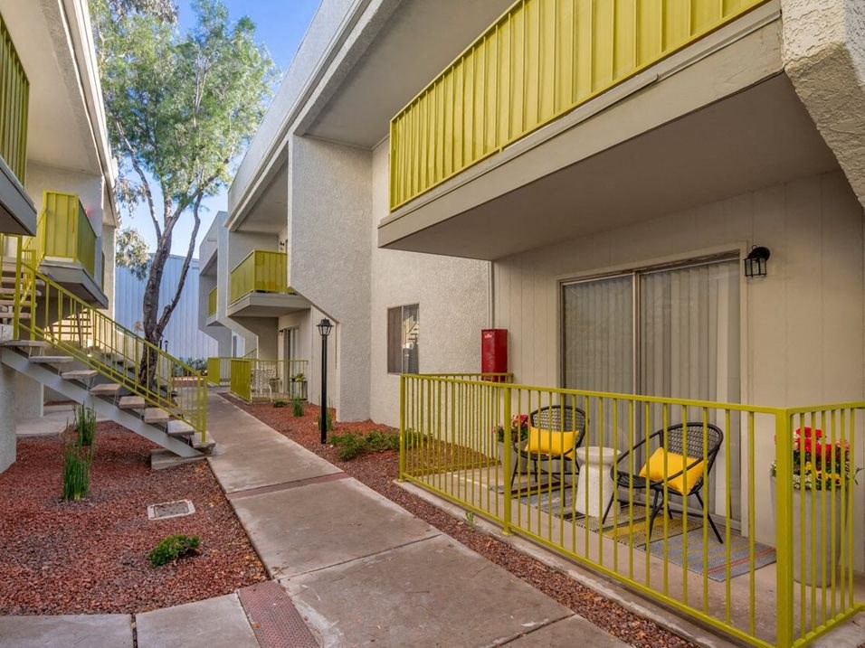 a patio with yellow chairs and a yellow railing in front of a white building with a yellow
