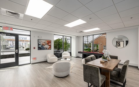A modern office space with a wooden table and chairs, a white bean bag, and a view of the city through the windows.