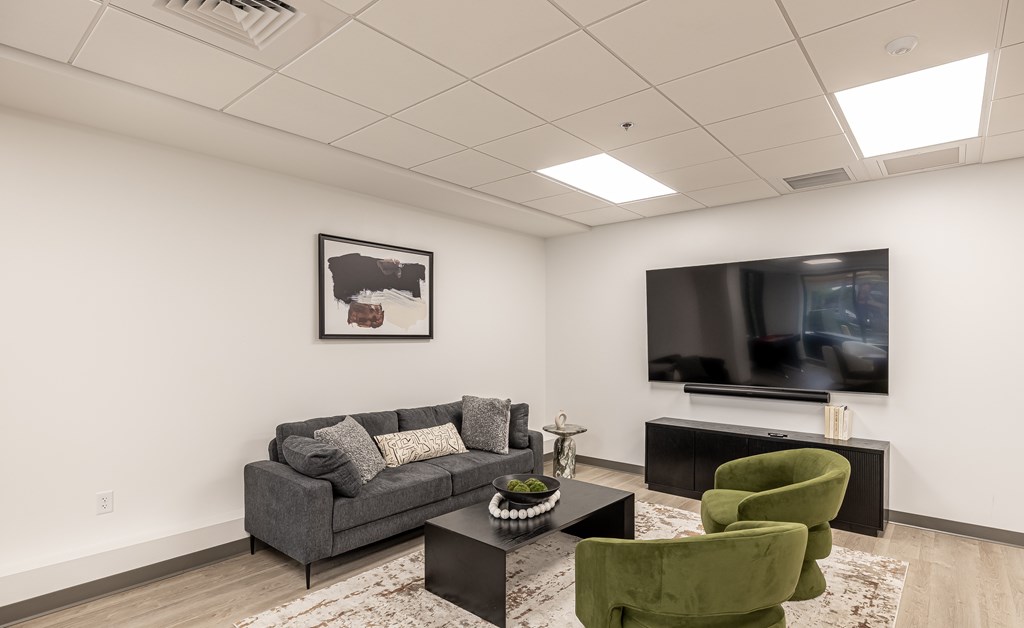 A living room with a grey couch, a green chair, and a flat screen TV mounted on the wall.