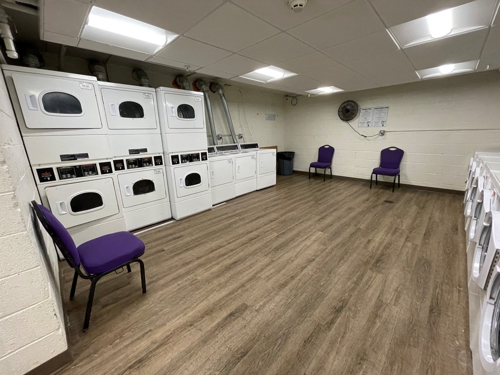 a large room with white washers and dryers and purple chairs