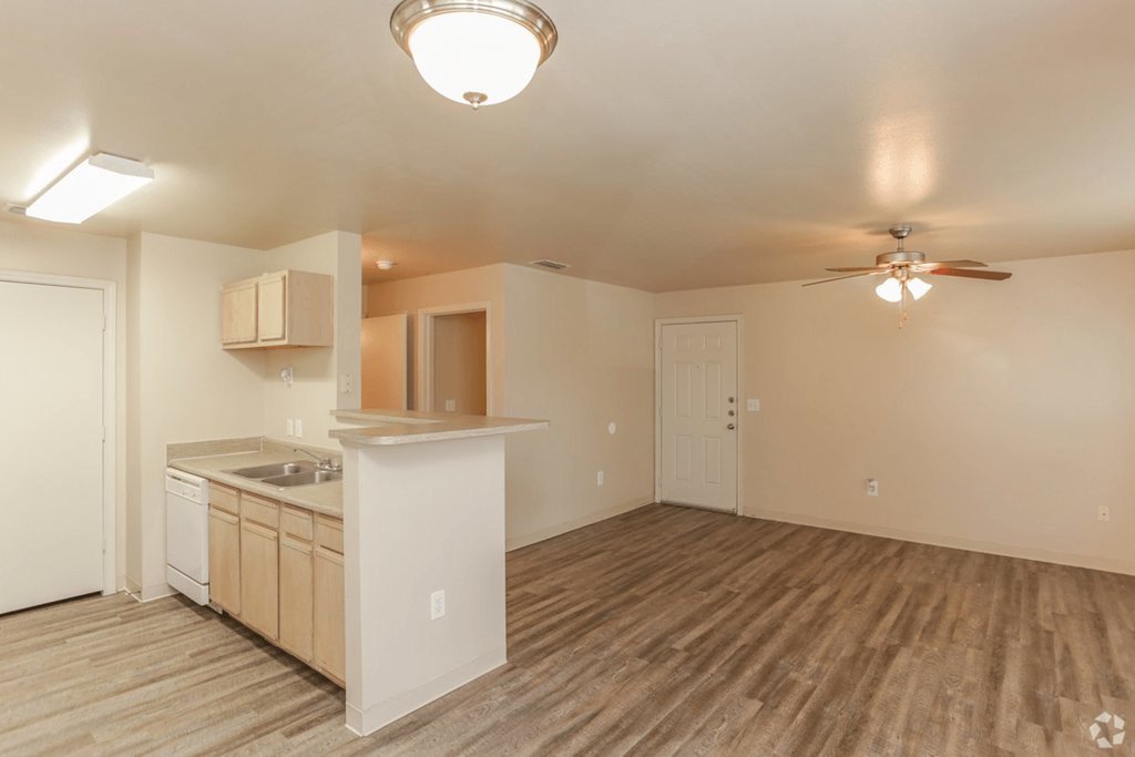 an empty living room with a kitchen and a ceiling fan