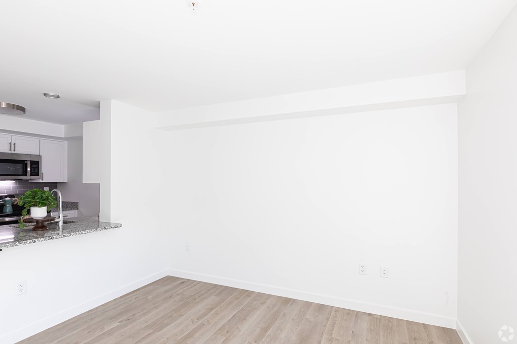 A white room with a wooden floor and a kitchen area to the left.