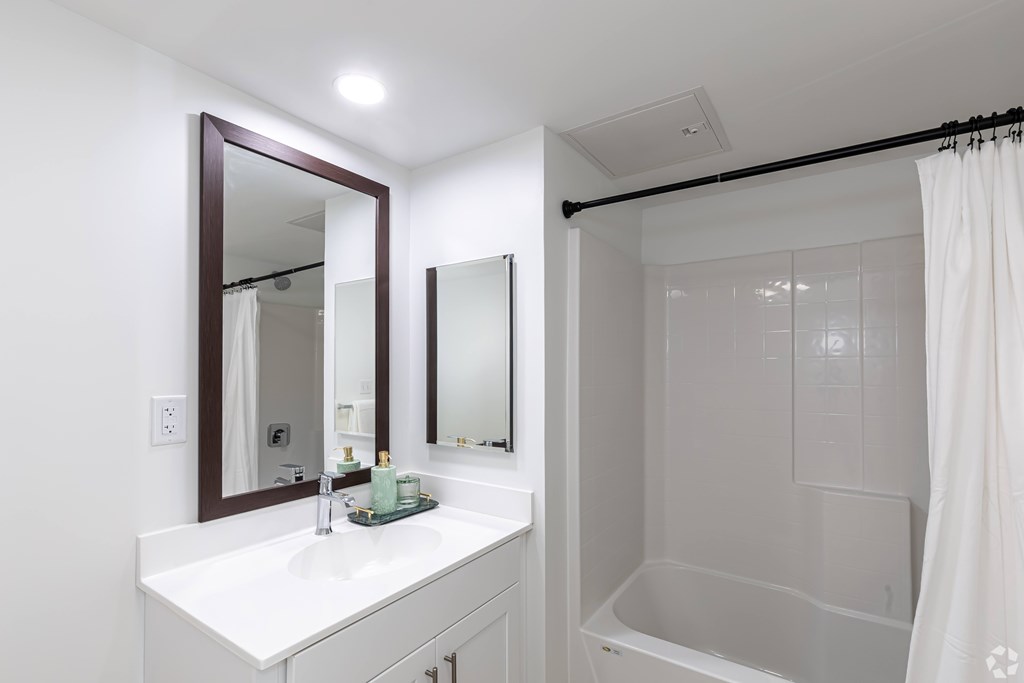 A white bathroom with a sink, mirror, and shower.