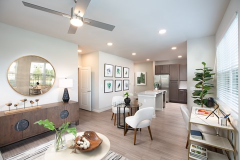 A modern living room with a round mirror, a dining table with chairs, and a kitchen area in the background.