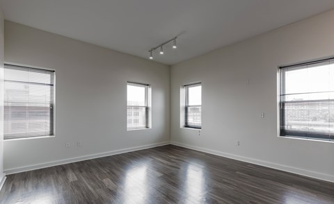 A spacious room with wooden floors and three windows.