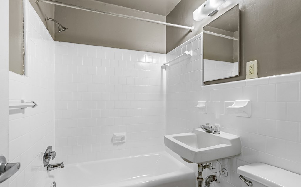 A white bathroom with a sink, mirror, and tub.