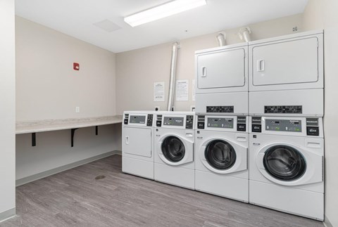 A laundry room with three washing machines and a bench.