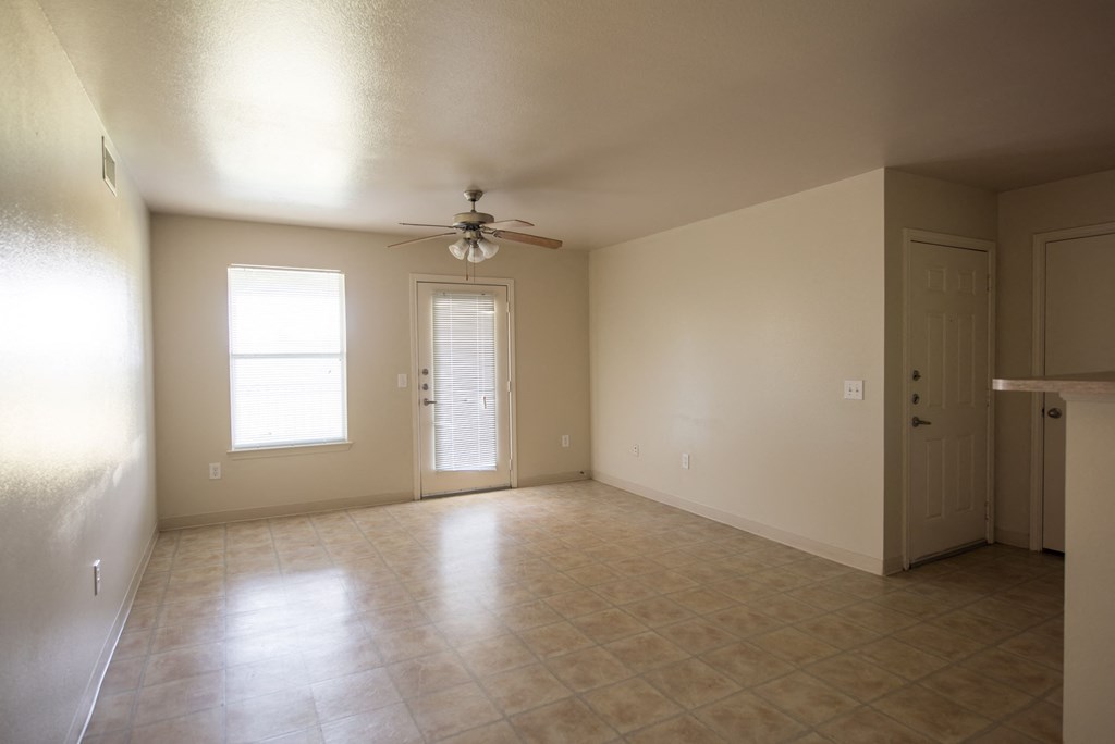 an empty living room with a ceiling fan and a door