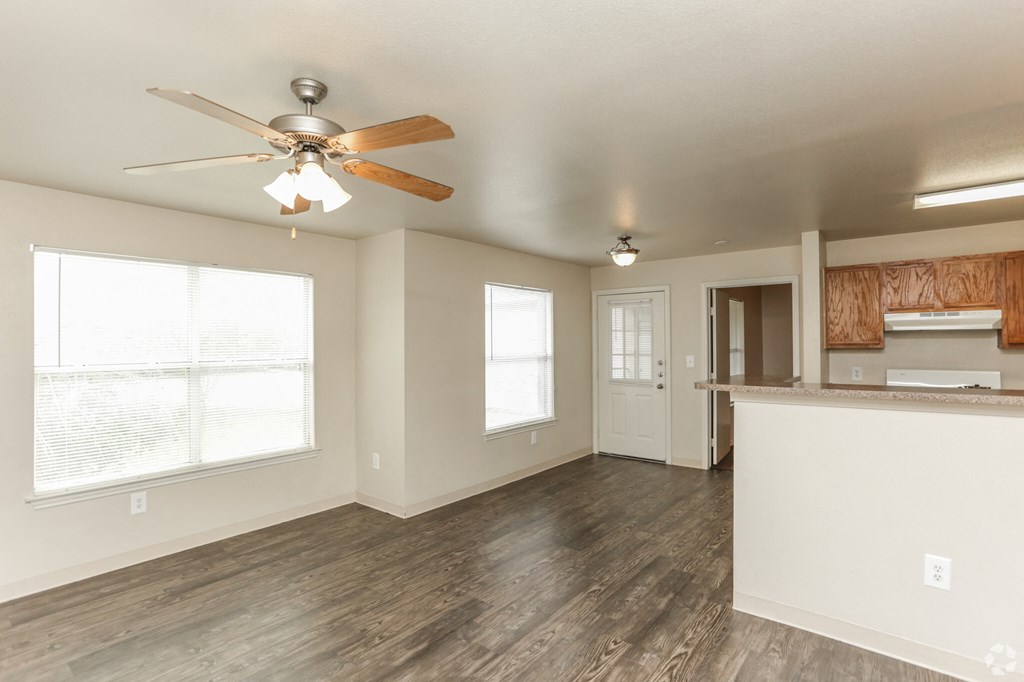 an empty living room with a ceiling fan and a kitchen
