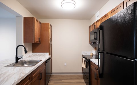 A kitchen with a black refrigerator and wooden cabinets.