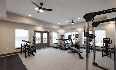 A gym with a variety of equipment including a treadmill, weights, and a squat rack at Hudson Heights Apartments, Mechanicville, NY