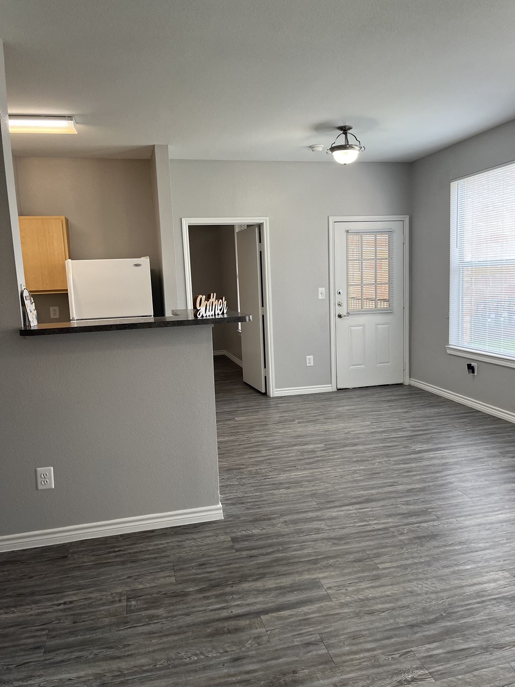 an empty living room with a kitchen and a white door