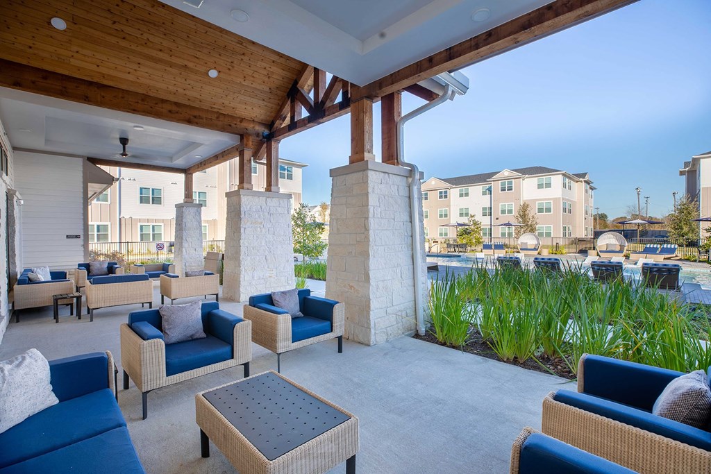 a patio with blue couches and chairs and a pool in the background at 55 Fifty at Northwest Crossing, Houston, TX