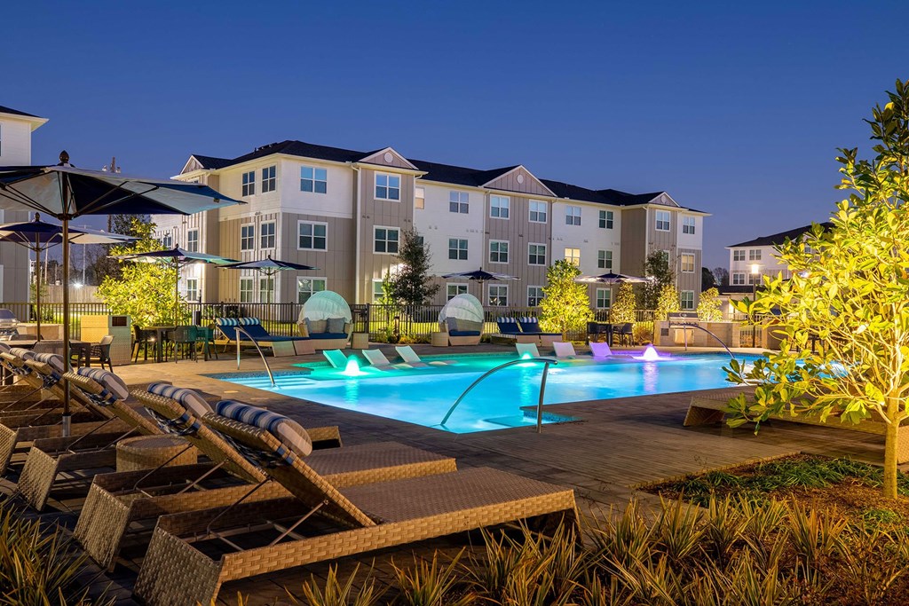a swimming pool with lounge chairs and umbrellas in front of an apartment building at 55 Fifty at Northwest Crossing, Houston, TX 77092