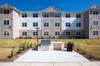 an outdoor patio with a grill in front of an apartment building at 55 Fifty at Northwest Crossing, Houston, TX