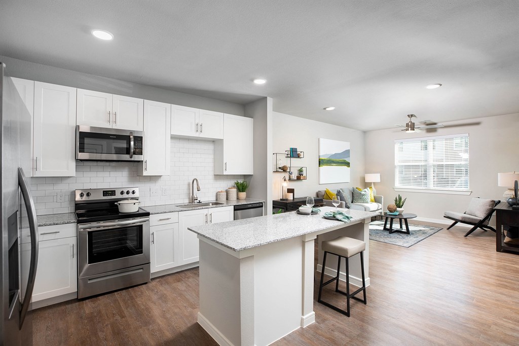a kitchen and living room with white cabinets and stainless steel appliances at 55 Fifty at Northwest Crossing, Houston Texas