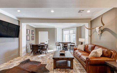 A living room with a brown leather couch and a cow skull mounted on the wall.