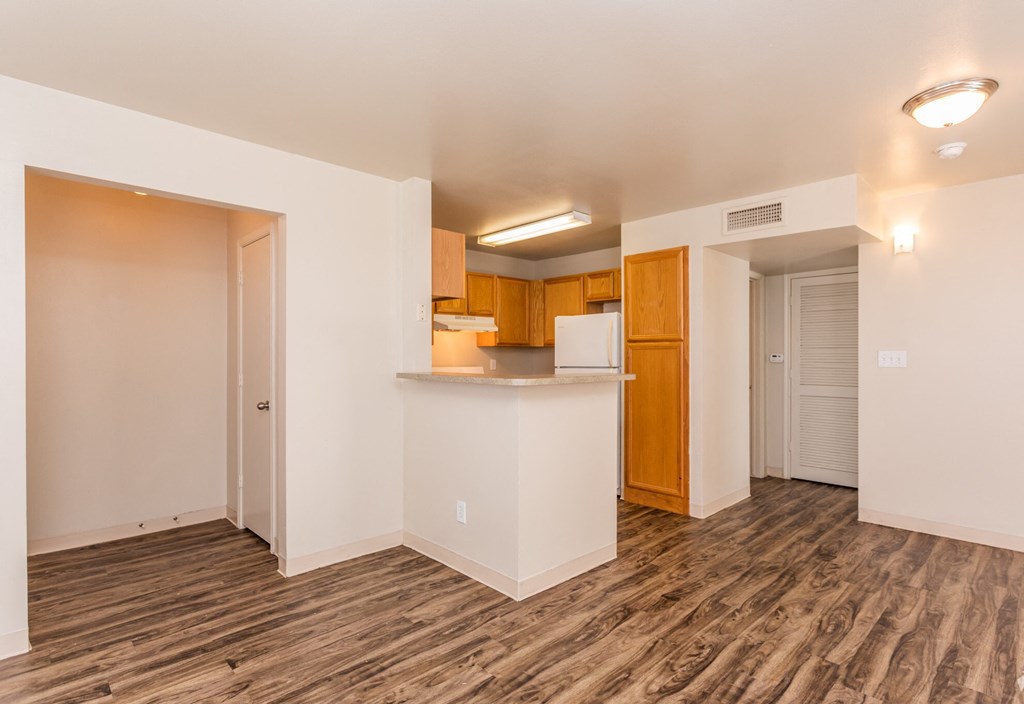 the living room and kitchen of an apartment with wood flooring and white walls