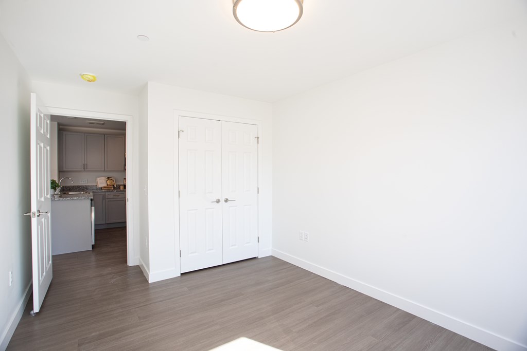 A kitchen with white cabinets and a white fridge is visible through the open door.