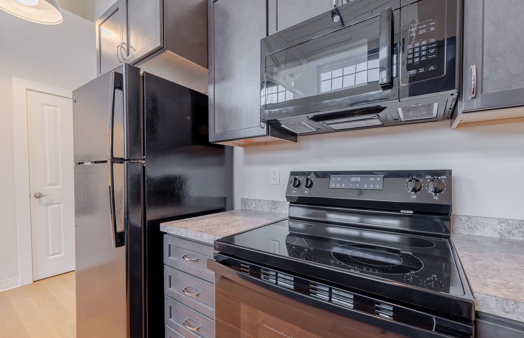 A black refrigerator is in a kitchen next to a stove and oven.