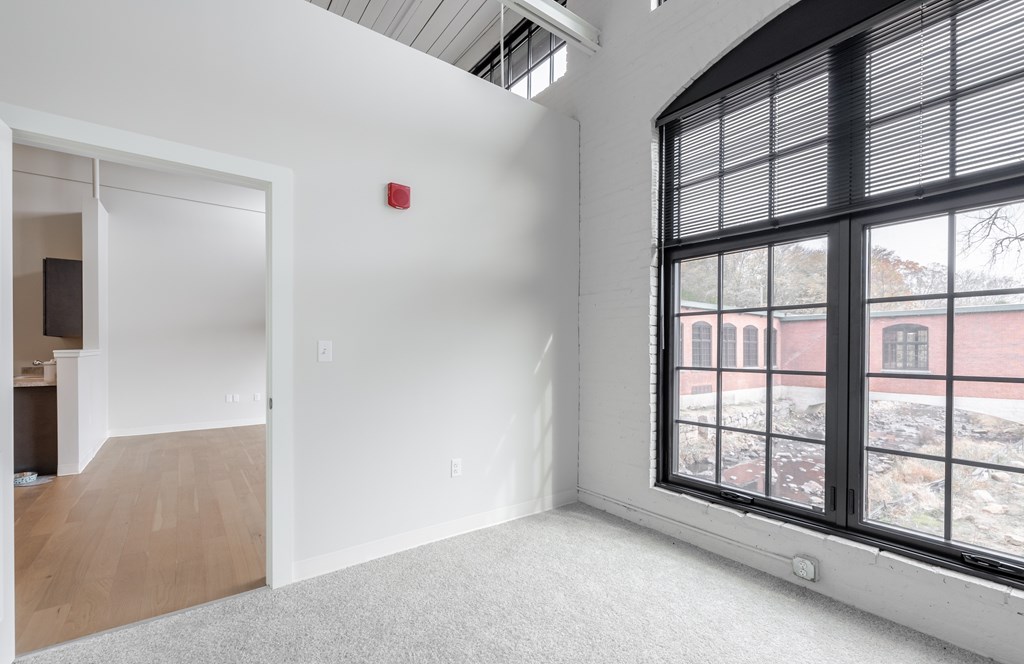 A room with a window and a fire alarm on the wall.