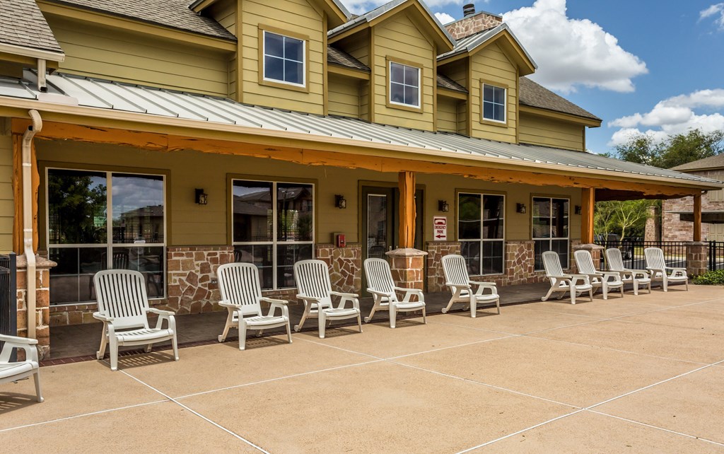 the porch of a yellow house with white rocking chairs