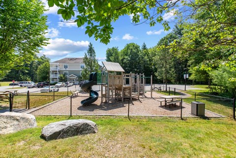 A playground with a slide and a wooden structure surrounded by a fence.