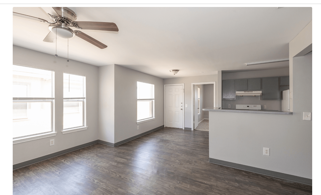 an empty living room with a ceiling fan and a kitchen