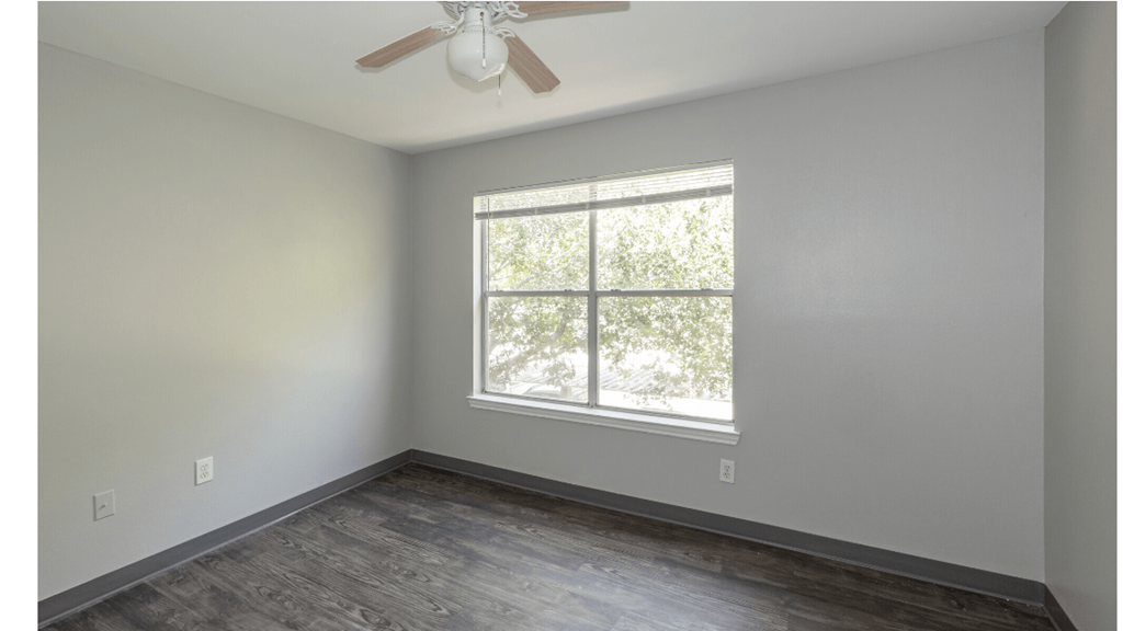 an empty bedroom with a large window and wood flooring