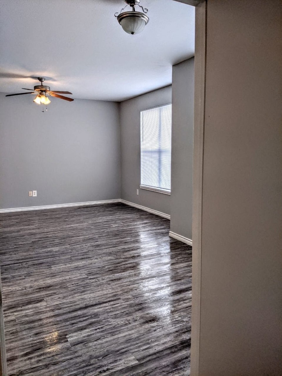 an empty living room with a ceiling fan and a window