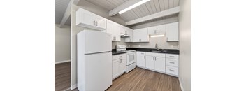 A white refrigerator is in a kitchen with white cabinets and a black counter.