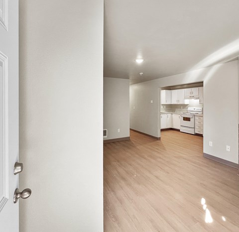 A room with a white door and a kitchen in the background.