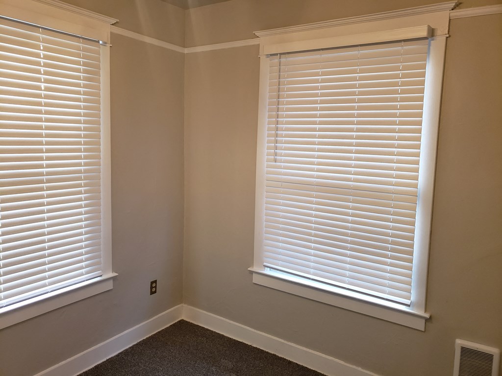 a corner of a room with two windows with white blinds
