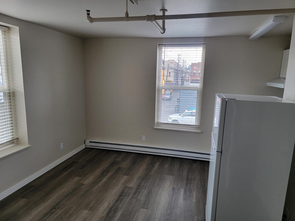 an empty room with a refrigerator and two windows