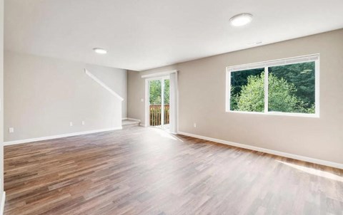 A spacious room with wooden flooring and a large window.