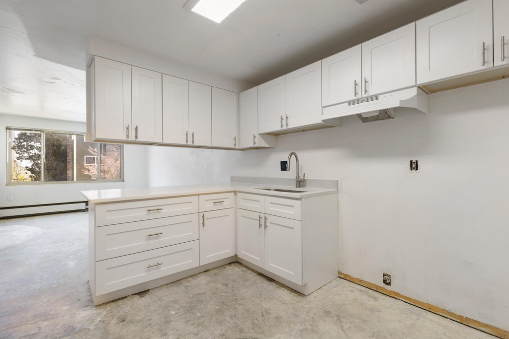 an empty kitchen with white cabinets and a sink and a window