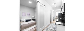 A bedroom with a bed, a television, and a kitchen area.