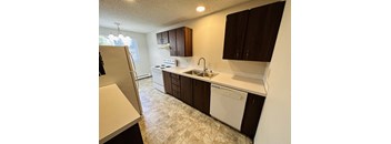 Galley-style kitchen with white appliances, dark wood cabinets, laminate countertops, and vinyl flooring in 1-bedroom Bridgeport Terrace apartment