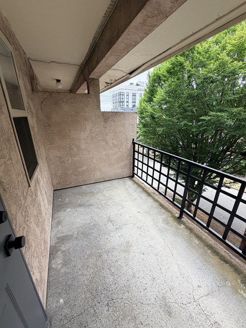 A balcony with a black railing and a view of a building and trees.