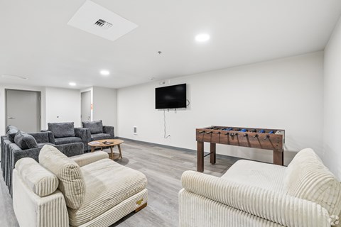 A living room with a white couch, grey couch, and a wooden table with a TV mounted on the wall.