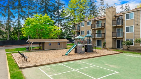 A playground with a slide and a basketball court in front of Hillcrest apartment buildings.