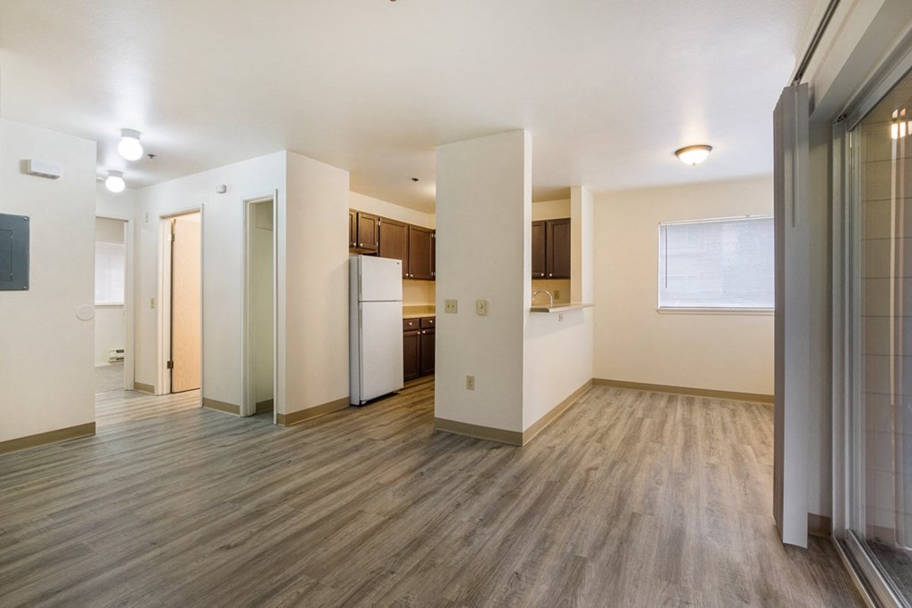 the living room and kitchen of an empty apartment with wood flooring and white walls