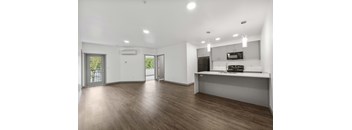 A spacious living room with a kitchenette and a view of the outdoors through a sliding glass door.