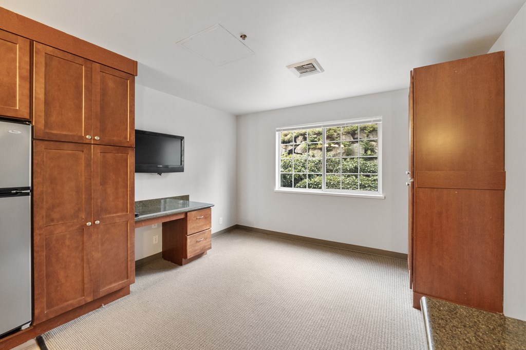 a room with a desk and a refrigerator and a window