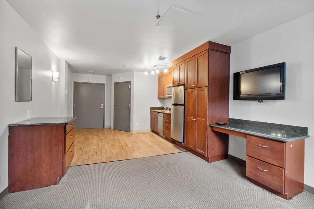 the living room and kitchen of an apartment with wood cabinets and a tv