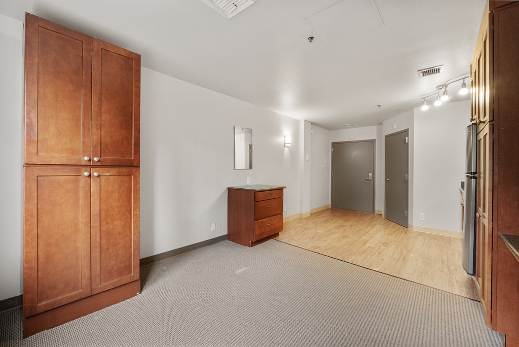 a living room with white walls and wooden furniture and a refrigerator