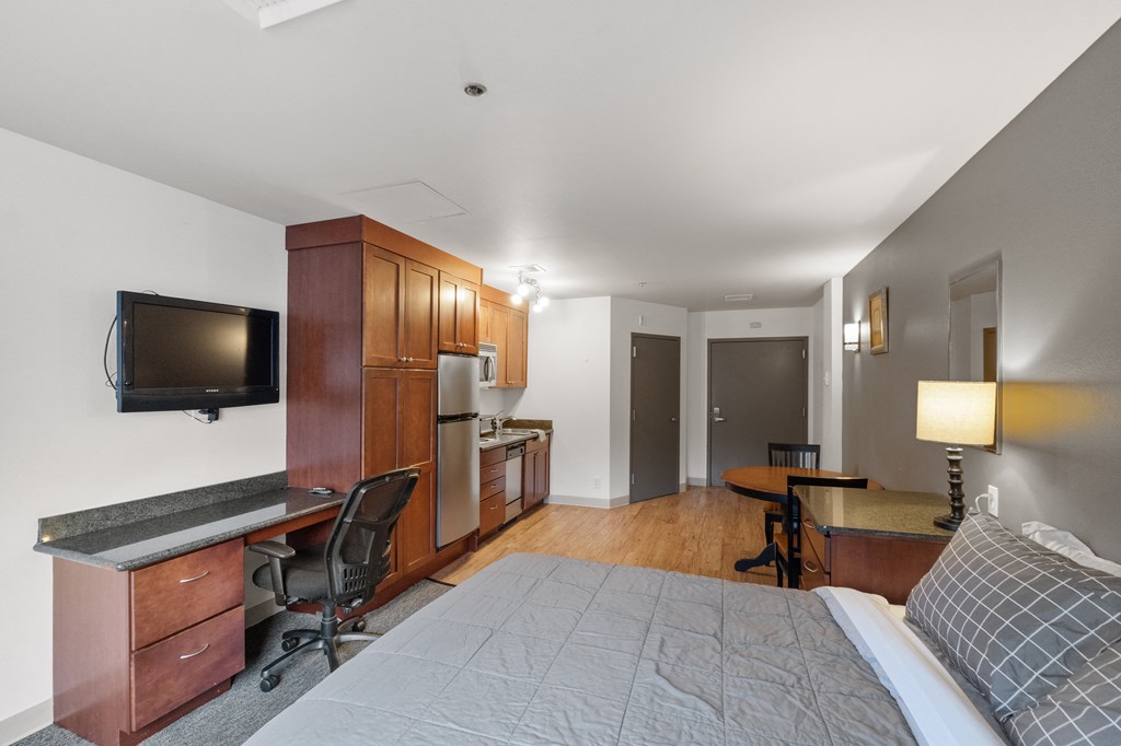 a bedroom with a bed and a desk and a kitchen with a tv