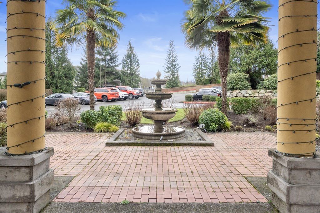 a fountain in a courtyard with palm trees and a parking lot